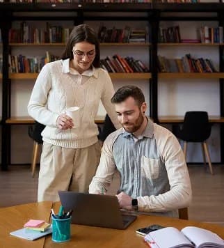 A colleague helping another at a desk in a library